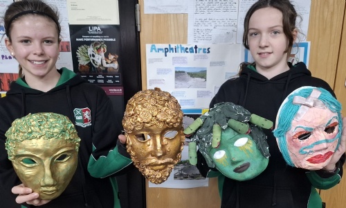 Two students holding the Greek masks that they have created